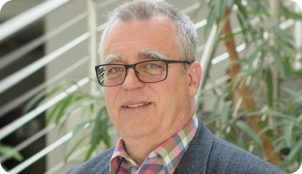 Dr. Wolfram Wendler, steht vor einer Pflanze und einem Treppengeländer.