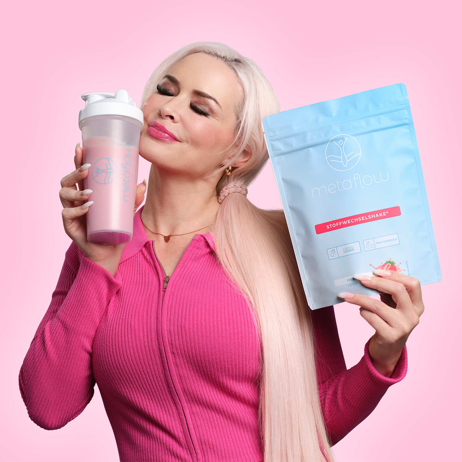 Daniela Katzenberger vor einem lila Hintergrund schaut zufrieden lächelnd, hält einen Metaflow Stoffwechsel-Shake Beutel in der einen Hand und einen Lila Shake in einem Metaflow Shaker in der anderen Hand 