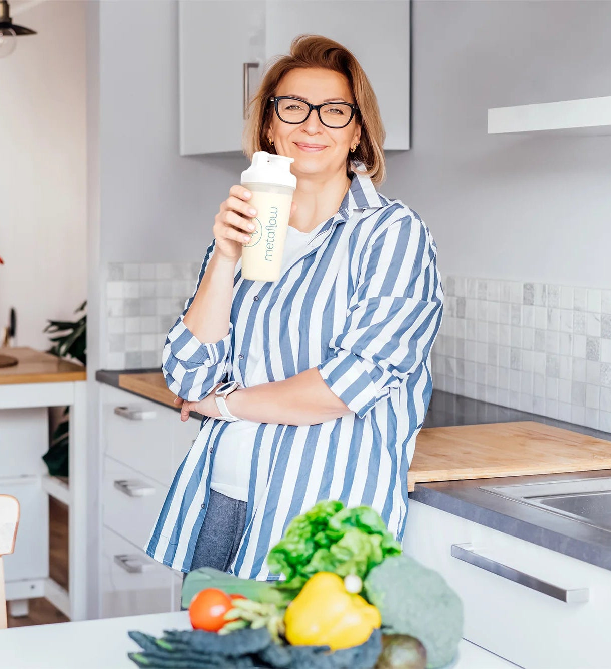 lächelnde Frau mittleren Alters steht in ihrer Küche und genießt einen Metaflow-Shake