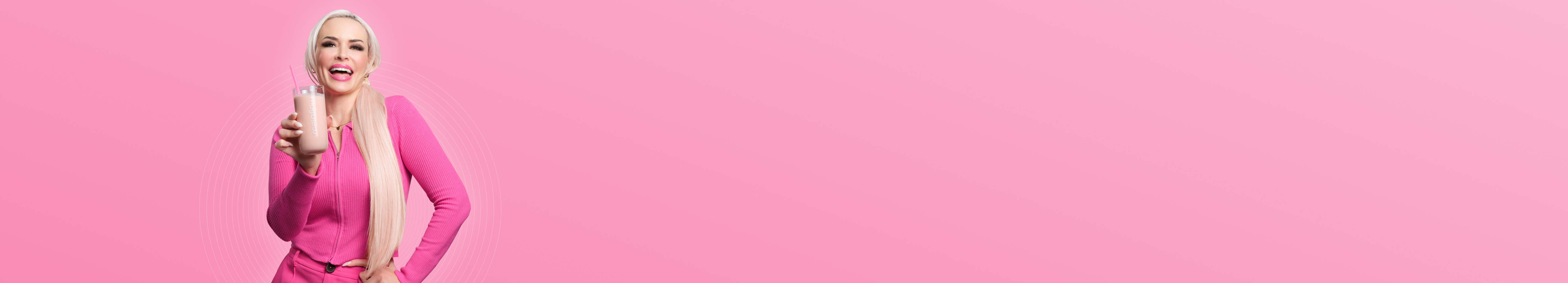 Daniela Katzenberger hält lächelnd vor einem lila Hintergrund einen lila Shake in der Hand